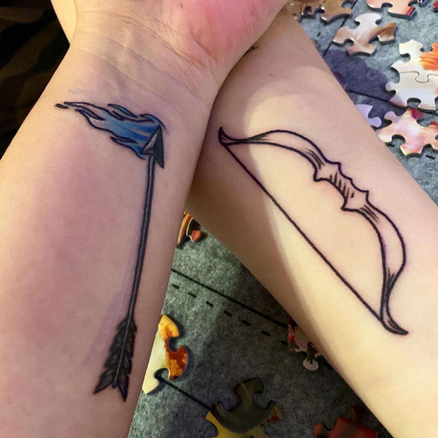 Two forearms with matching tattoos, one shows a flaming arrow, the other shows a bow